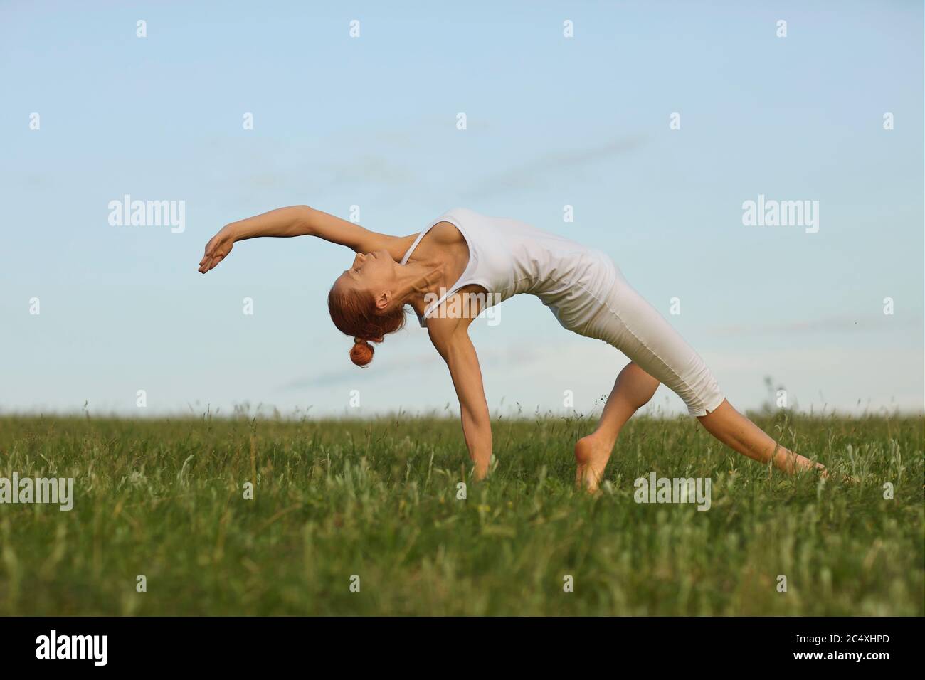 Yoga balance in nature. Graceful young woman practicing backbend yoga pose on green meadow. Fit girl standing in bridge position outdoors Stock Photo