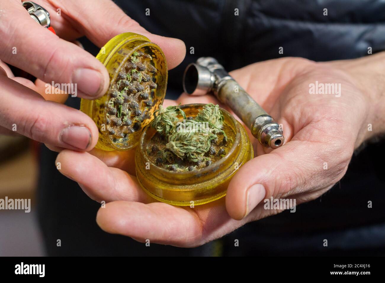 Male hands holding a marijuana grinder full of marijuana about to be used and a smoking pipe. Stock Photo