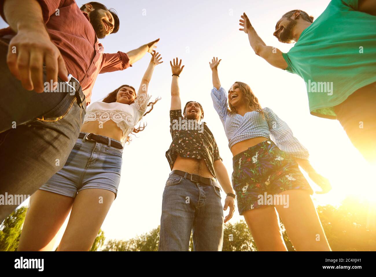 Group of young friends raising their hands in unity, low angle view. Happy people celebrating victory outdoors Stock Photo
