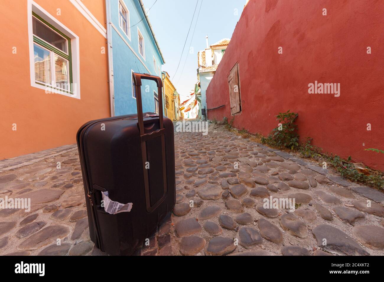 Black troler suitcase on an empty medieval city street. Colorful buildings and stone paved street with blue sky. Travel concept. Stock Photo