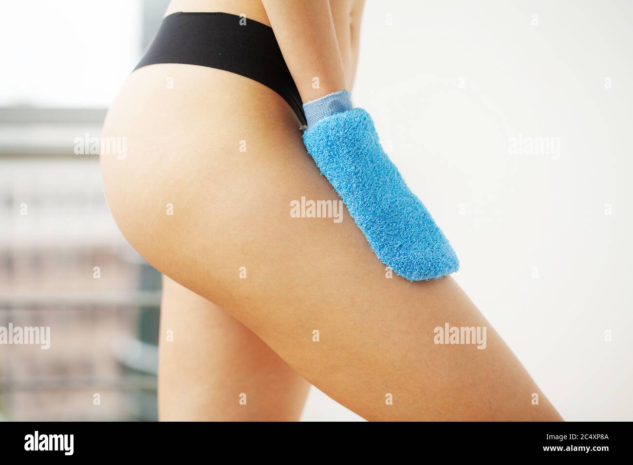 Woman arm holding blue dry brush to top of her leg, cellulite treatment