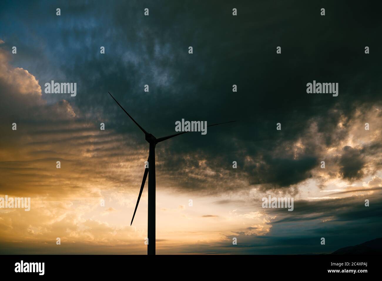 The silhouette of a high industrial wind turbine against the sunset sky ...