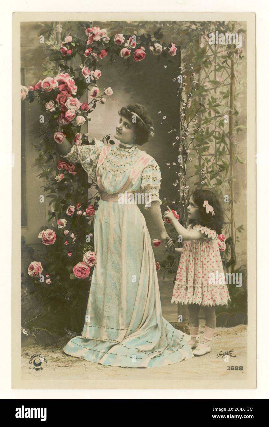 Early 1900's antique French sentimental tinted greetings postcard - mother and cute daughter holding her hand picking roses, France, circa 1912 Stock Photo