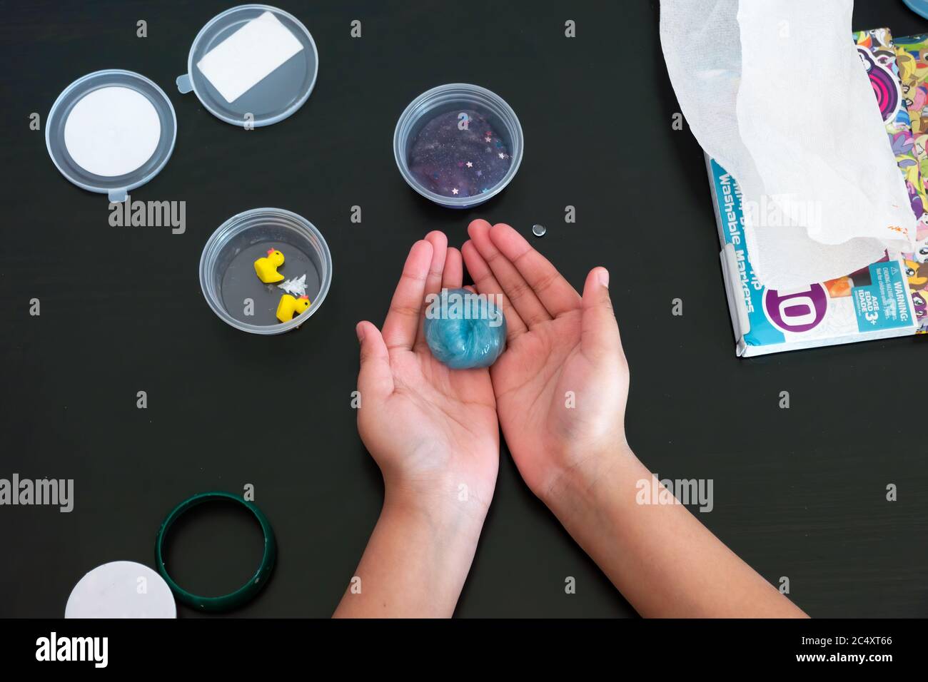 A view from above of a young girl playing with the Slime on a table and has it compressed into a circular shape.. Stock Photo