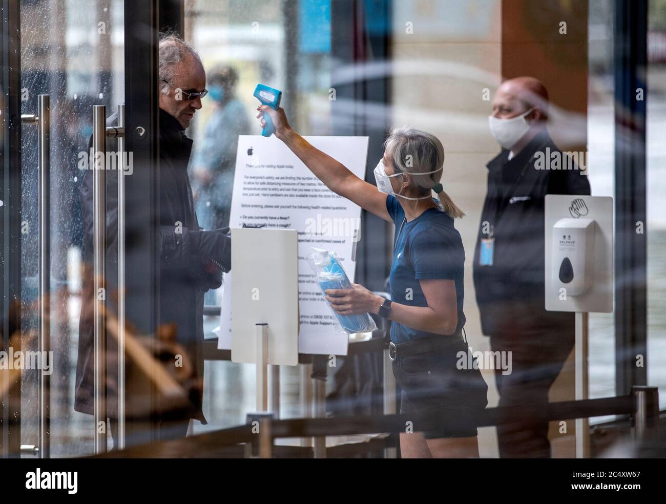 A member of staff at the Apple store in Edinburgh's Princes Street takes the temperature of a customer before entering as non-essential stores across the country reopen today as part of Scotland's phased plan to ease out of the coronavirus pandemic lockdown. Stock Photo