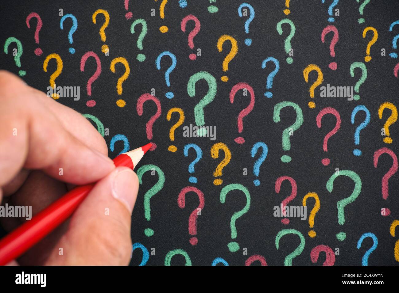 Man drawing colorful question marks with a pencil on black paper. Close