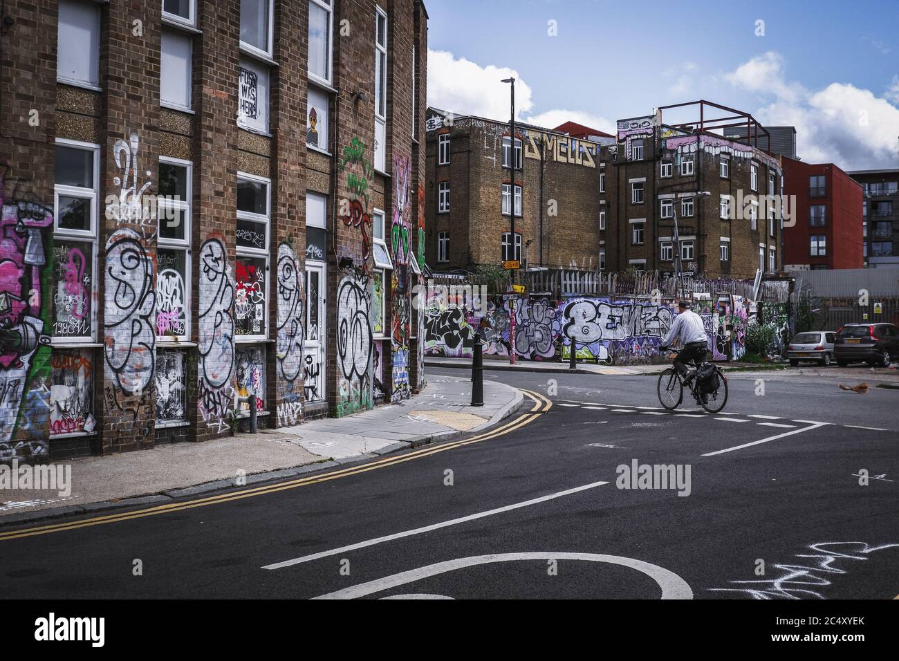 man rides a bike past graffiti on a derelict building in Hackney Wick in East London,during covid-19 lockdown Stock Photo