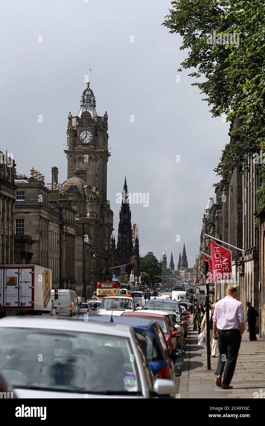 Princes Street, Edinburgh with car traffic, iconic Balmoral Hotel and Scott Monument in the background. Pedestrians and tourists walking on sidewalk. Stock Photo