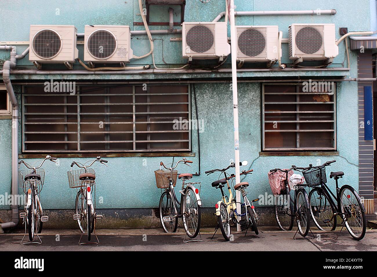 Bicycles parked in front of turqoise wall with ventilation in Japan. Stock Photo