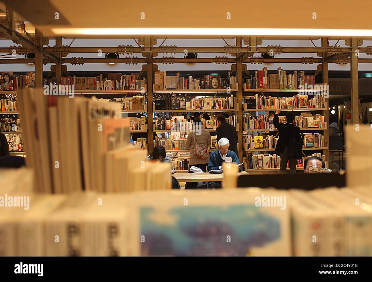 Tokyo, Japan: A Japanese bookstore with people browsing shelfs and sitting and reading. The scene is shot through book shelves with blurry covers. Stock Photo