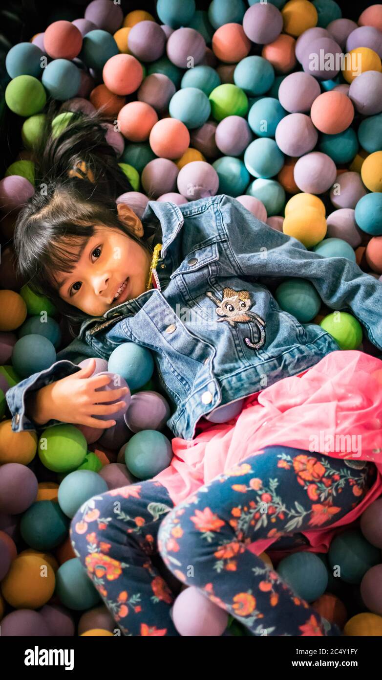 Little asian girl having fun in ball pit with colorful balls. Child