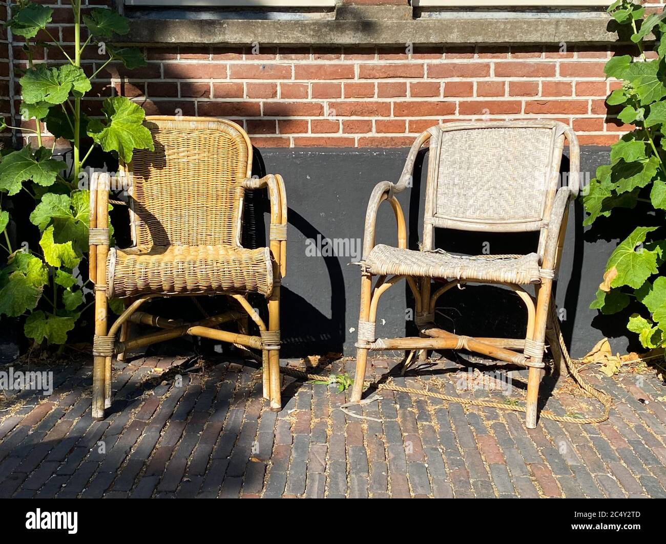 View on two empty old braided rattan chairs, brick wall background ...