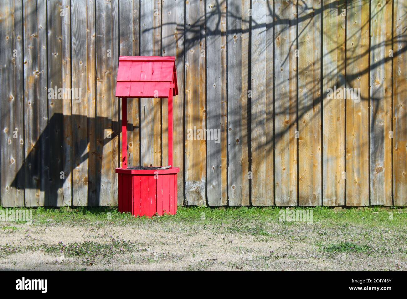 a very bright red wishing water well in front of a brown fence and grass Stock Photo