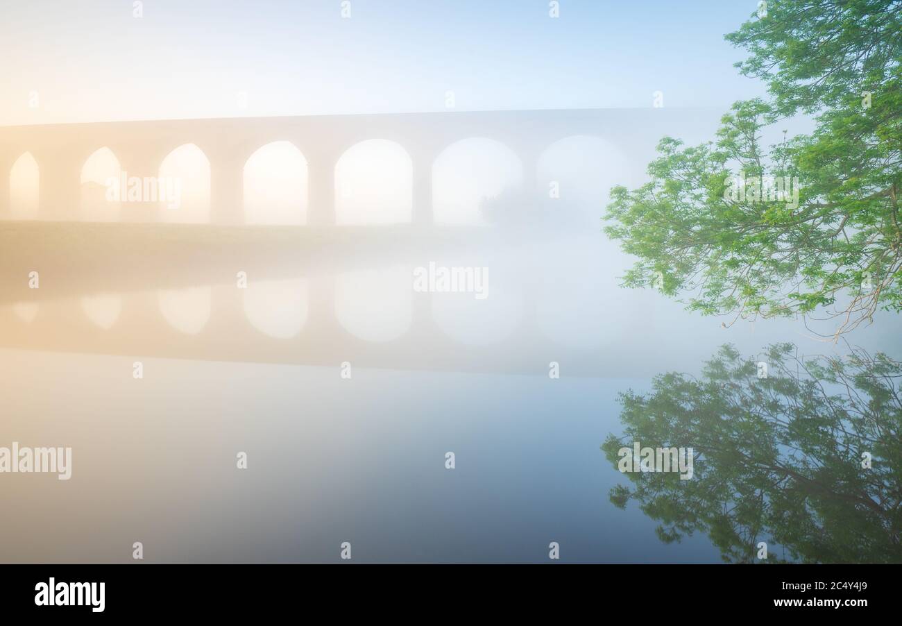 Arthington Viaduct is just visible through early morning mist on a late spring morning, the River Wharfe perfectly reflecting the railway arches. Stock Photo