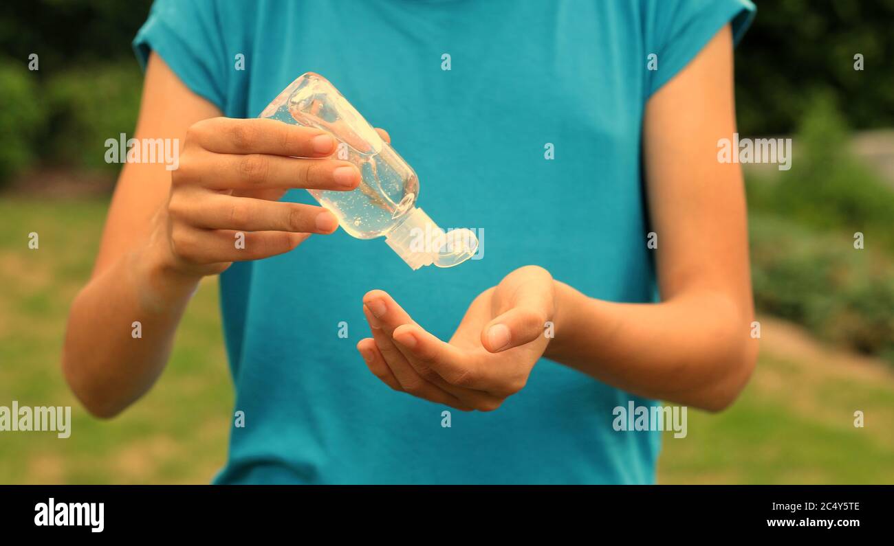 Young woman wearing a protective face mask desinfecting her hands with sanitizer in a bottle to prevent getting ill from influenza or corona disease Stock Photo