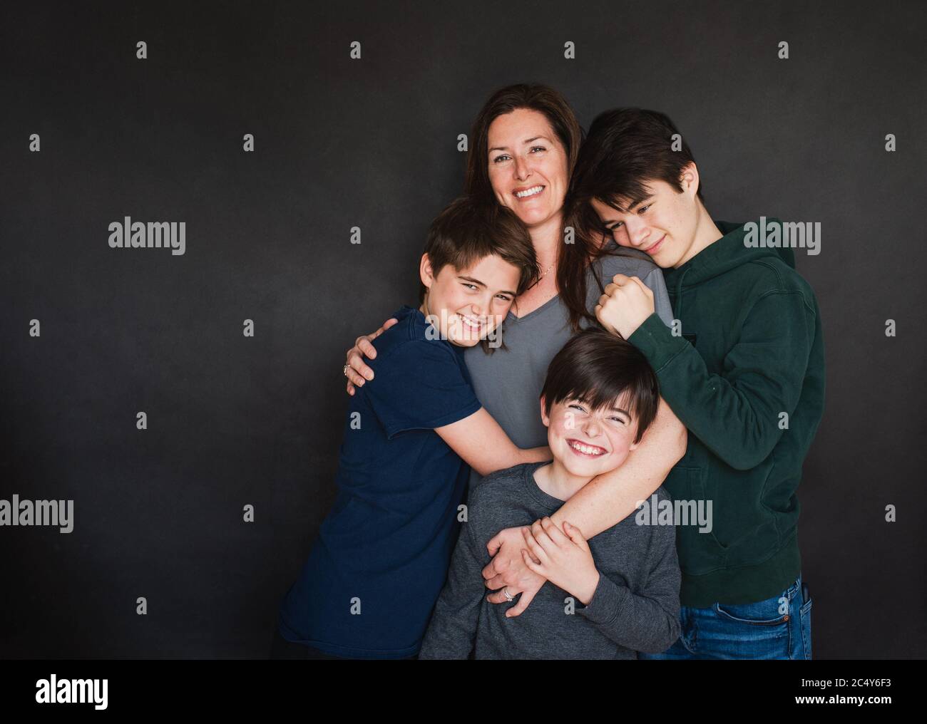 Mother with three older boys hugging against black backdrop. Stock Photo