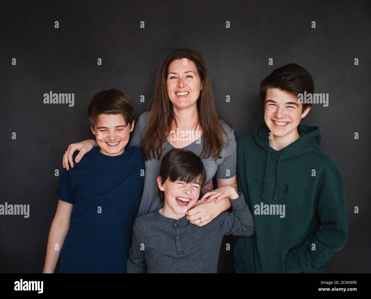 Mother with three older boys laughing against black backdrop. Stock Photo