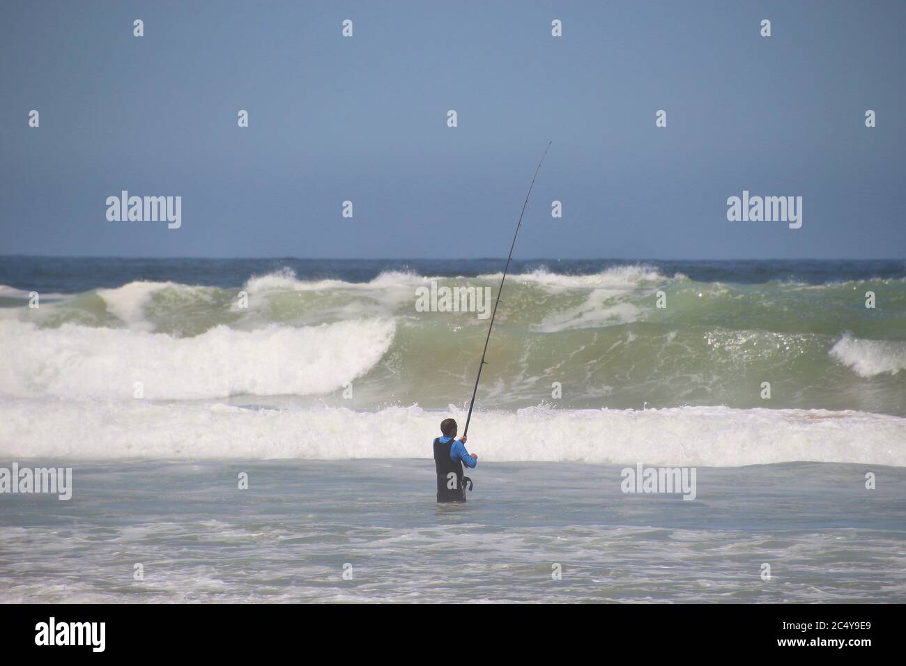 Plettenberg Bay, South Africa: A Fisher stands in the water, in front of huge waves of the wild Indian ocean. Garden Route, South Africa. Stock Photo