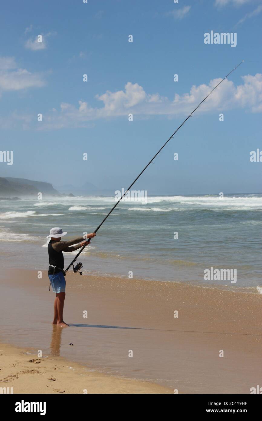 Plettenberg Bay, South Africa: A Fisher stands in the water, in front of huge waves of the wild Indian ocean. Garden Route, South Africa. Stock Photo