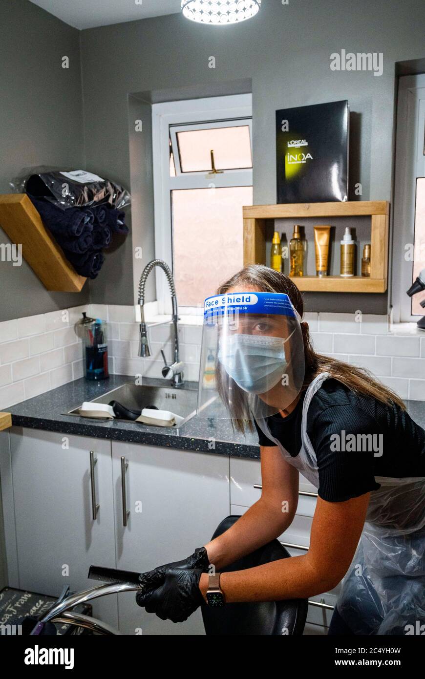 Female hairdresser wearing PPE including a face shield gloves and apron