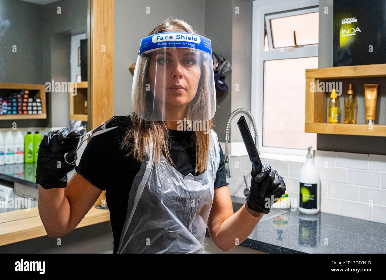 Female hairdresser wearing PPE including a face shield gloves and apron