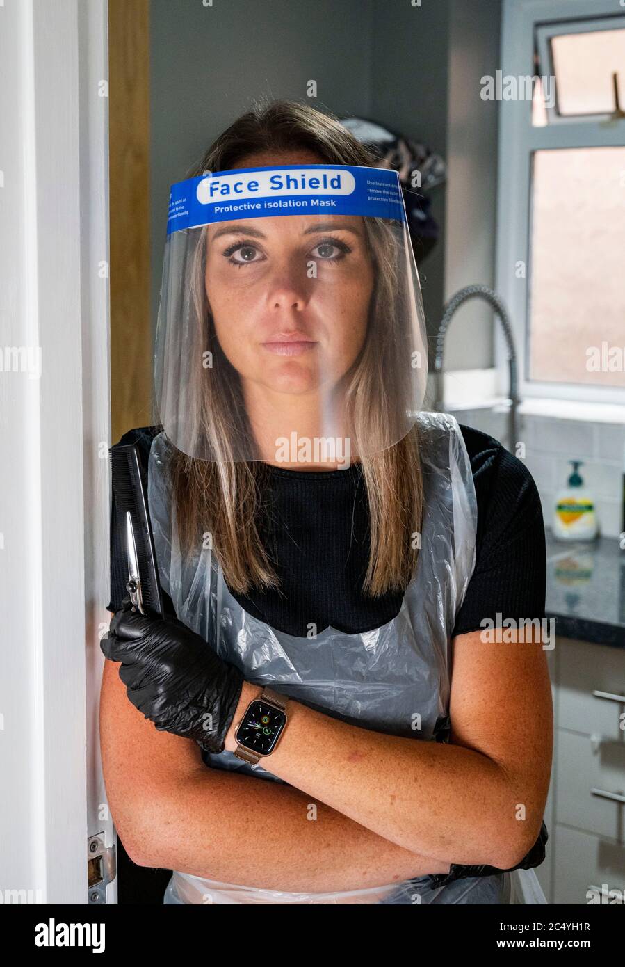 Female hairdresser wearing PPE including a face shield gloves and apron
