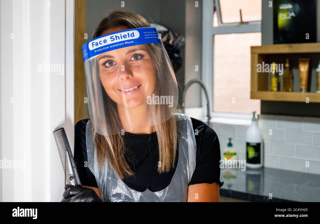 Female hairdresser wearing PPE including a face shield gloves and apron