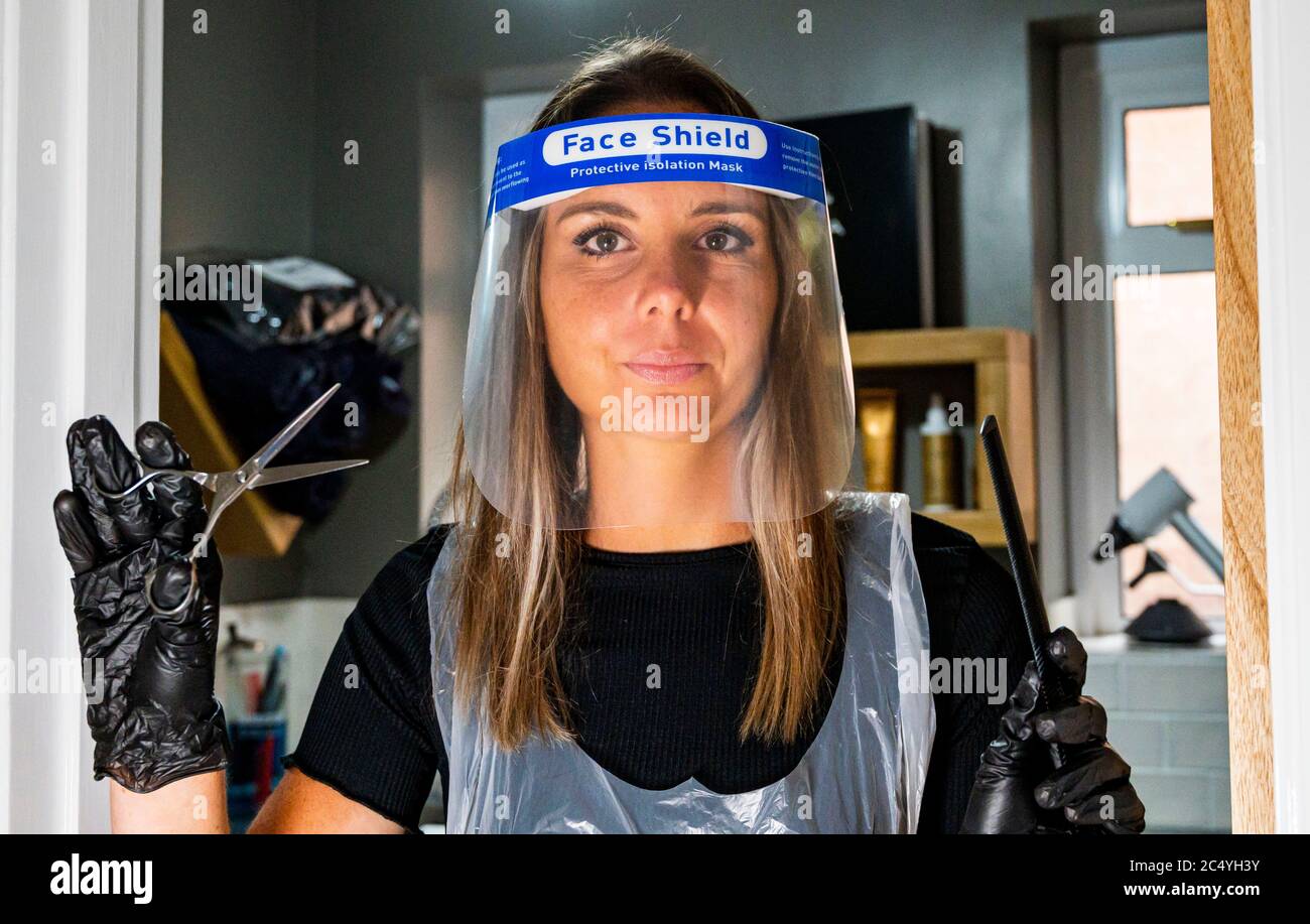 Female hairdresser wearing PPE including a face shield gloves and apron
