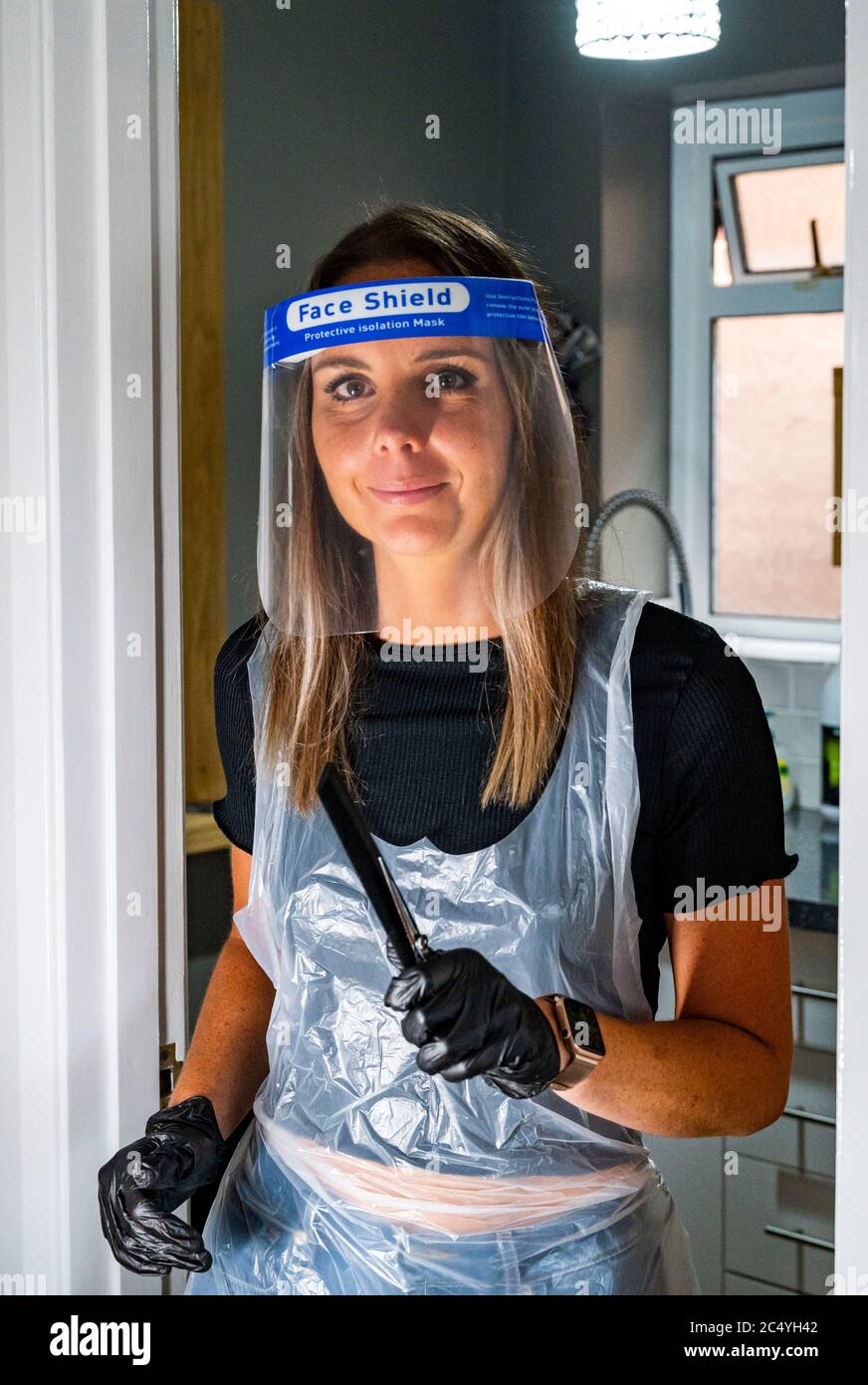 Female hairdresser wearing PPE including a face shield gloves and apron