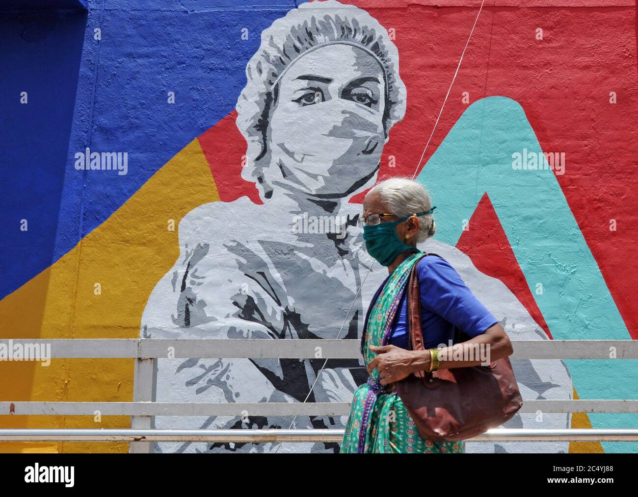 An elderly woman walks past a graffiti of coronavirus warrior in Mumbai.Mural depicts a nurse as one of the many corona warriors who have worked throughout the lockdown, exposing themselves to the risk of infection. It is the expression of what every citizen is thankful for the efforts of essential service providers in the face of rising covid-19 cases. Stock Photo