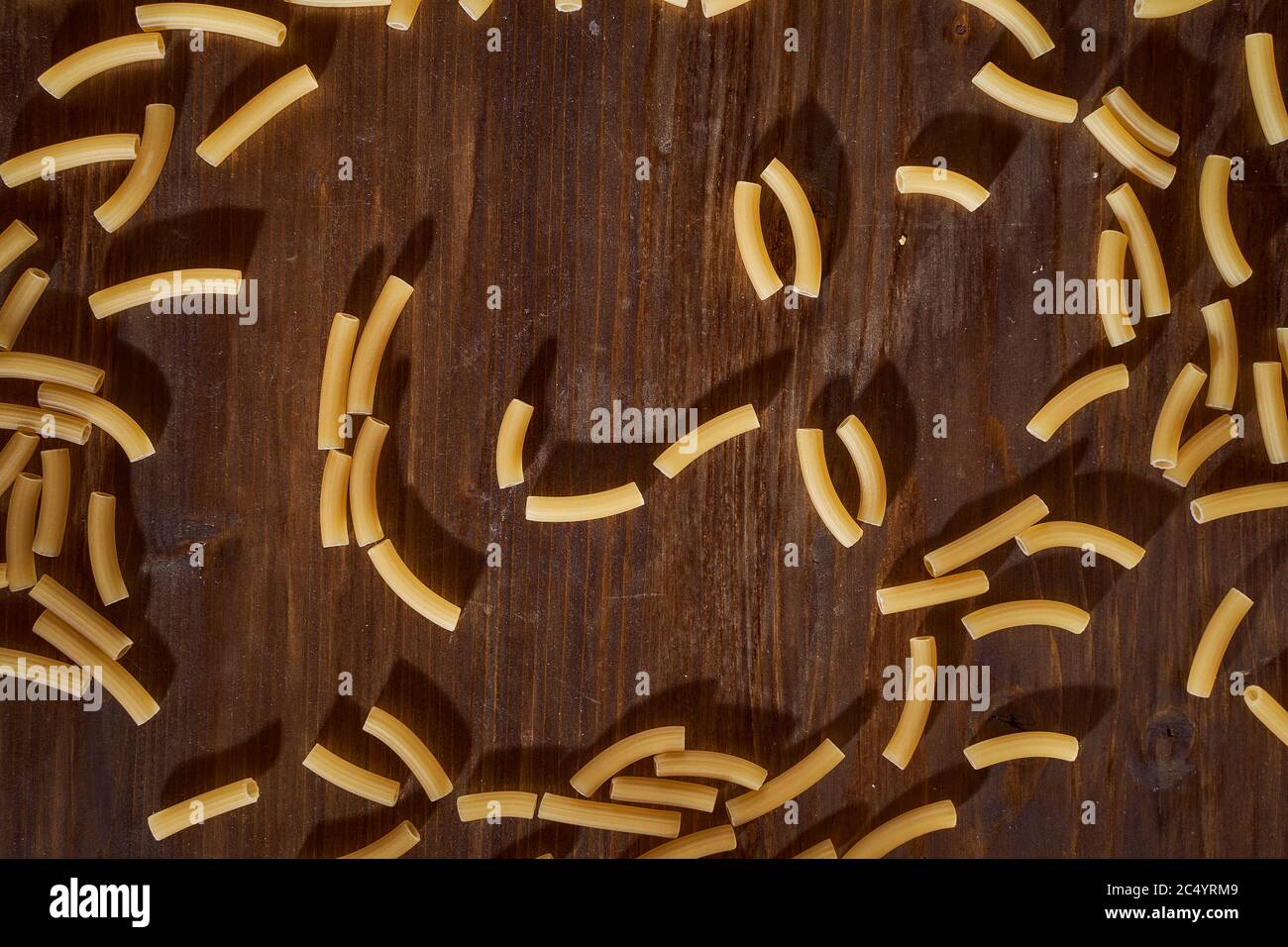 Yellow pasta in a shape resembling a human face lies on a brown table. Close-up. Stock Photo