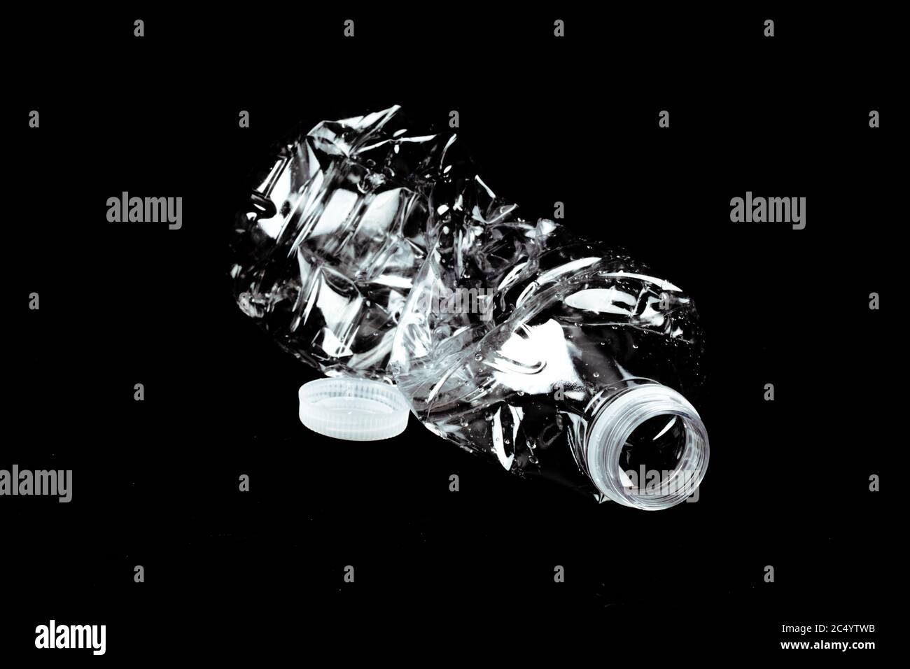 a single crushed empty clear plastic single use water bottle garbage on a black background Stock Photo