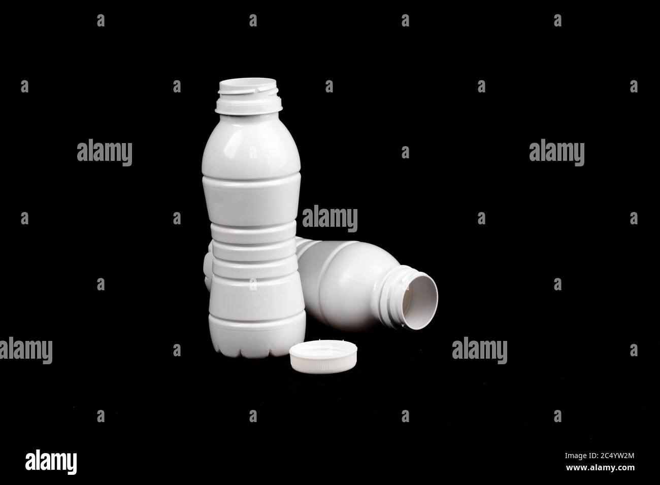 two empty white plastic single use milk bottles on a black background Stock Photo