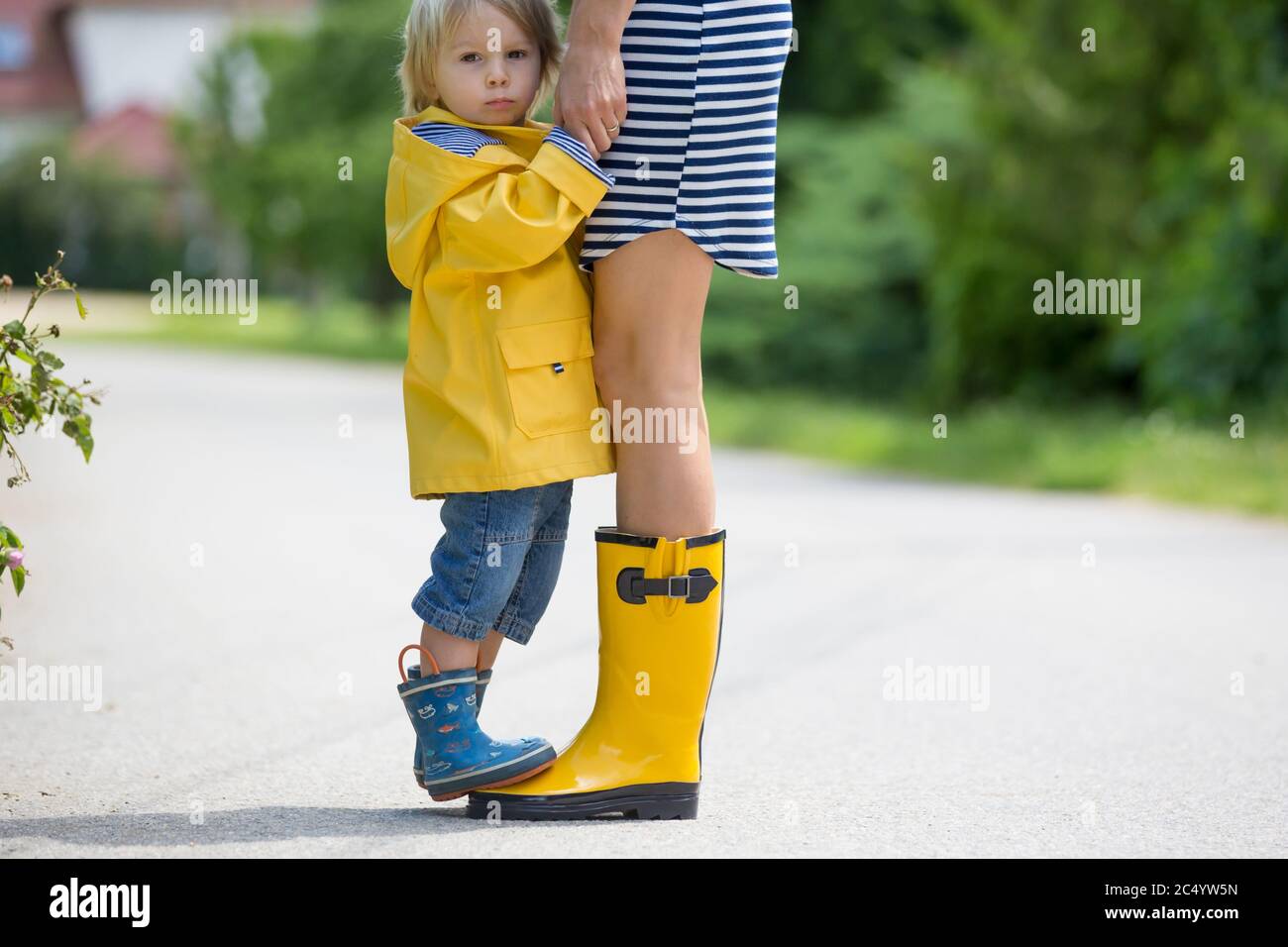 Mother and toddler child, boy, playing in the rain, wearing boots and