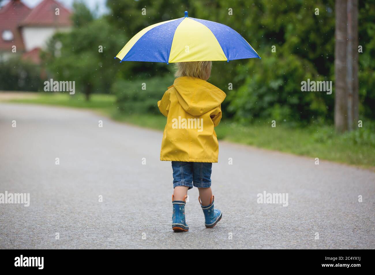 Mother and toddler child, boy, playing in the rain, wearing boots and