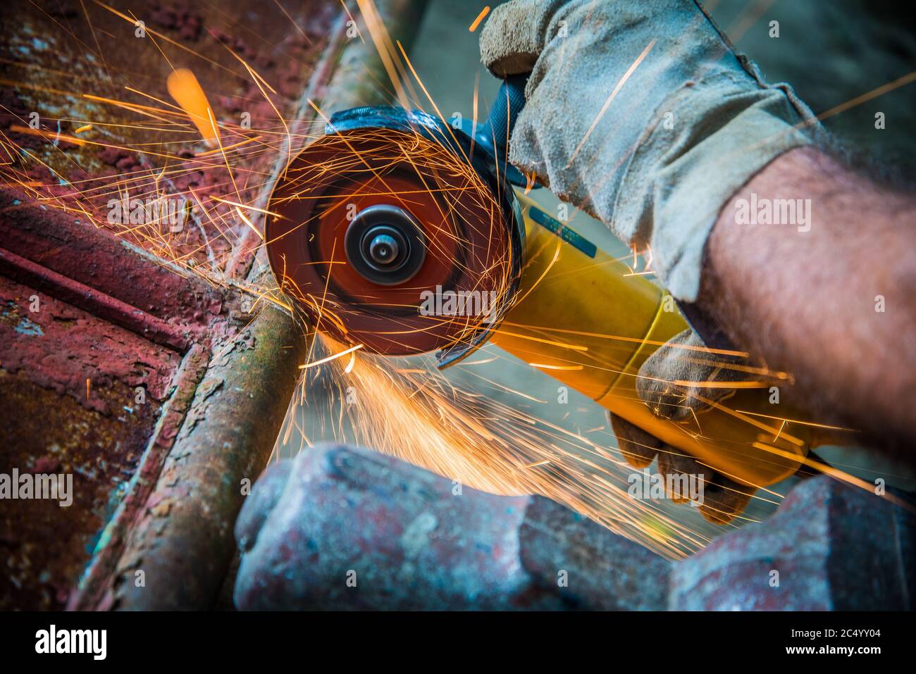 Worker cutting metal with electric wheel grinder in factory. Sparks while grinding iron. Close up view Stock Photo