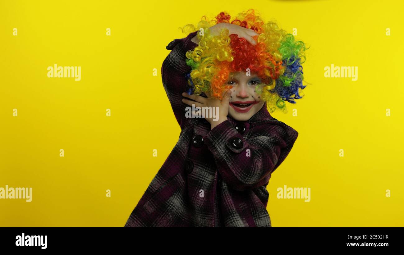 Little caucasian child girl clown in rainbow wig making silly faces. Five years old female kid