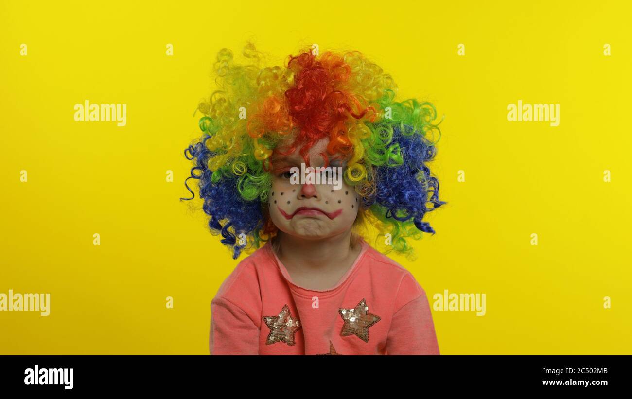 Child girl clown in colorful wig making silly faces. Happy five years old little caucasian kid