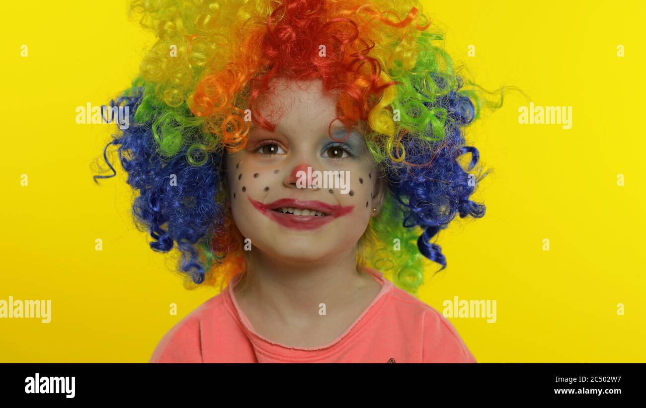 Child girl clown in colorful wig making silly faces. Happy five years old  little caucasian kid having fun, smiling, dancing, looking at camera.  Expressions. Halloween. Yellow background. Chroma Key Stock Photo -
