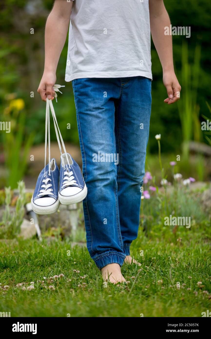 Preteen child, holding pair of sneakers in his hands, walking on a rural path, barefeet Stock Photo