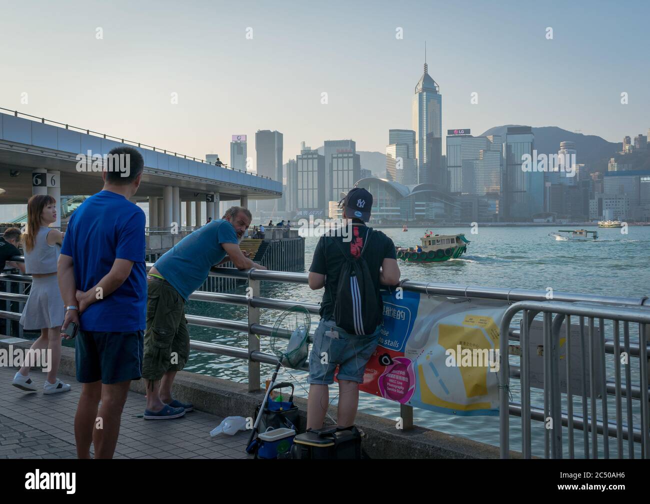A caucasian man fishing by the Star Ferry Pier in Kowloon Tsim Sha Tsui with a view of Hong Kong island across the harbour. Stock Photo