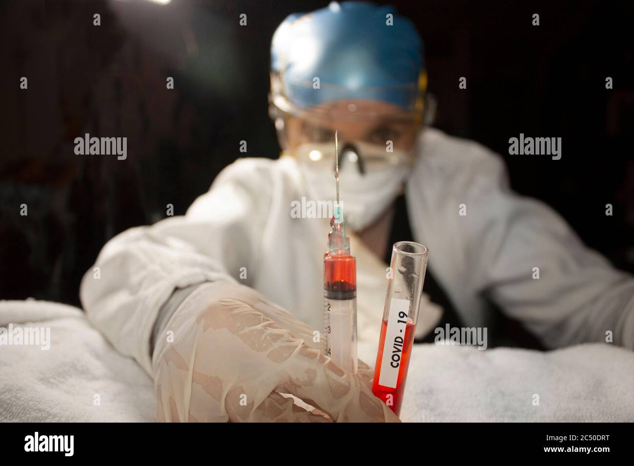 Scientist's hand equipped with gloves, glasses, mouths, holding test tube and syringe containing covid-19 plasma for study of possible vaccine in Stock Photo