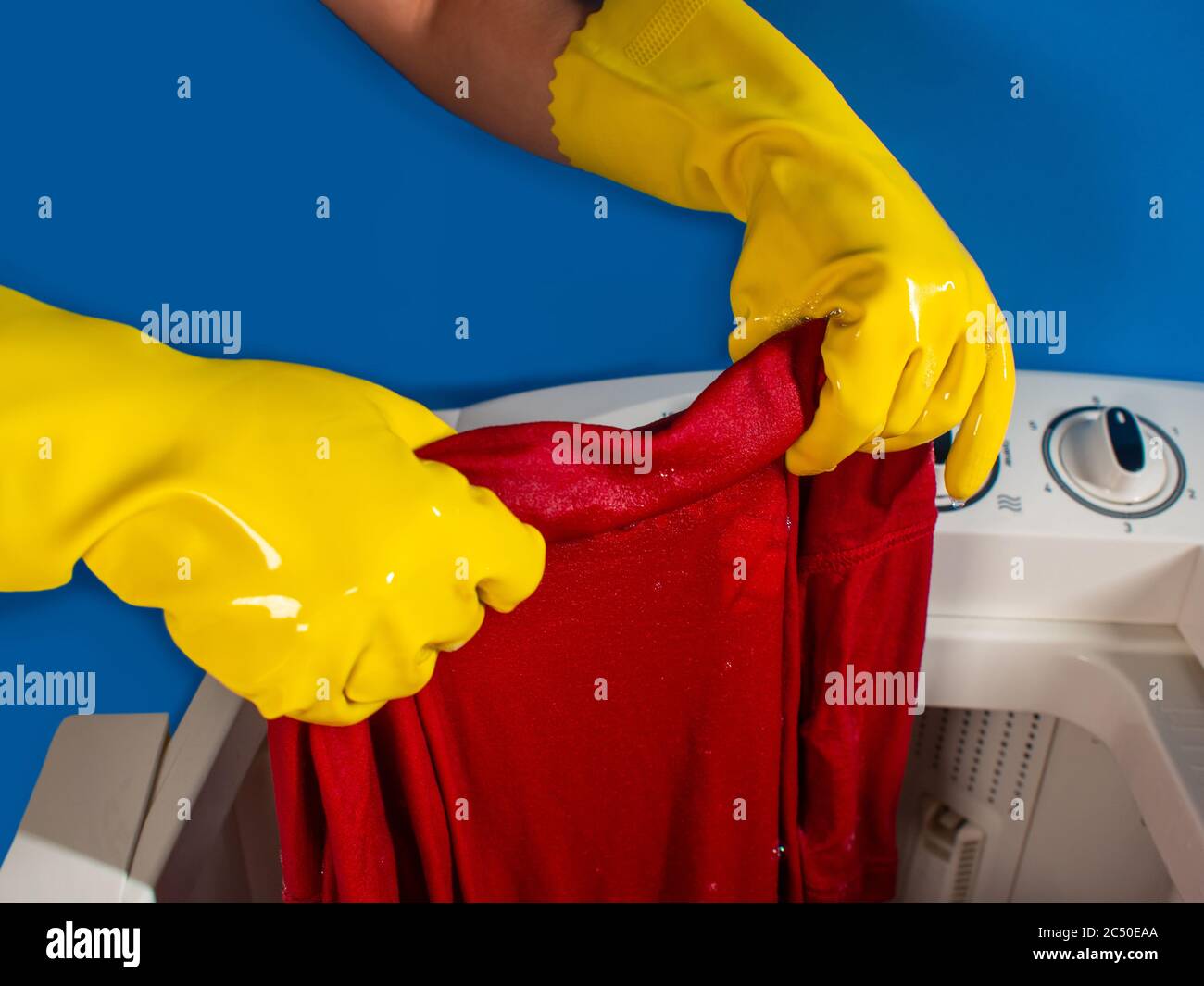 girl hands with yellow cleaning gloves taking out a red shirt from washing machine and blue background Stock Photo