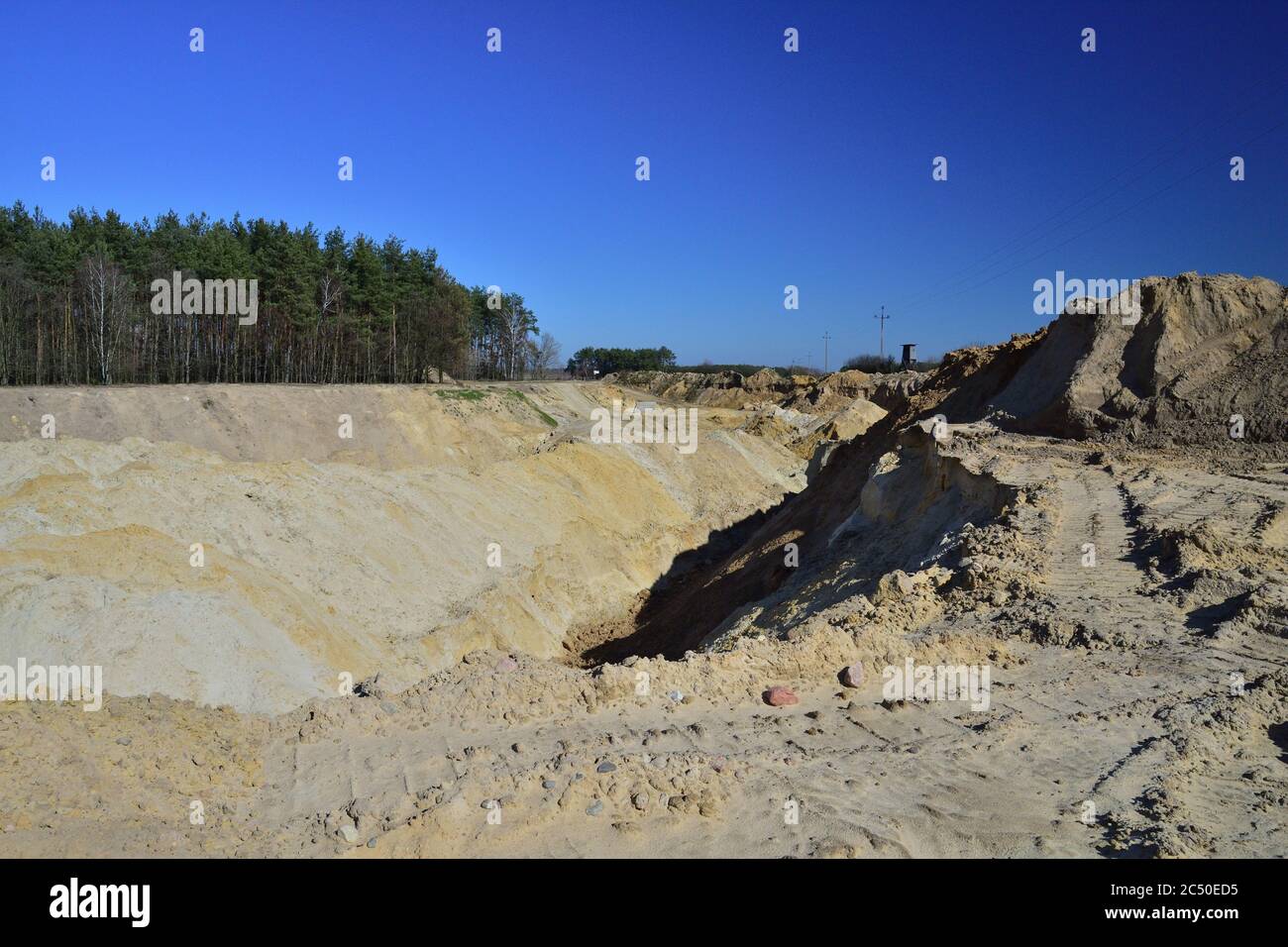 A sand mine in the sharp light of the midday sun. On the horizon of trees. Stock Photo