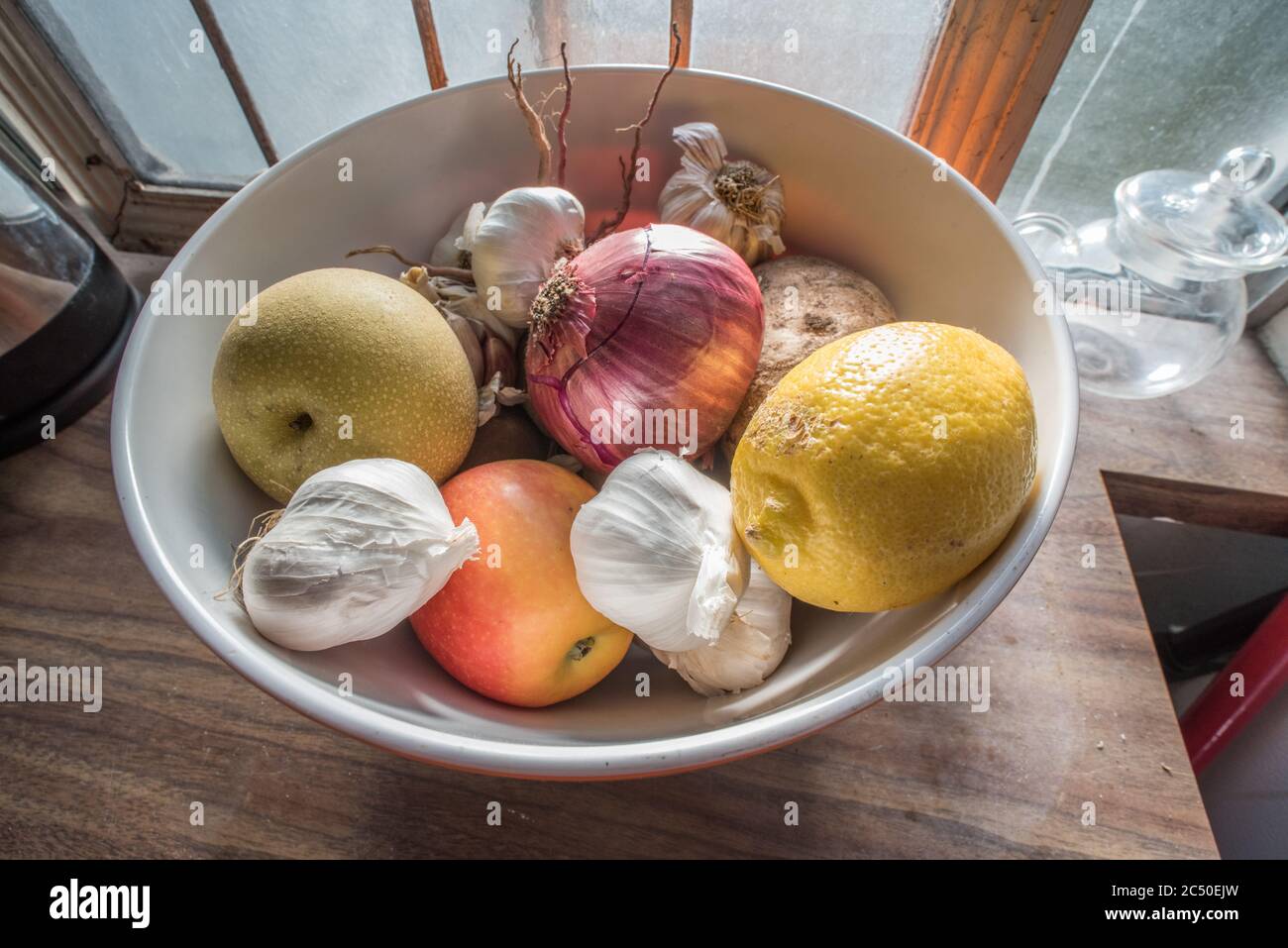 A still life of a bowl of mixed fruit and vegetables sitting on a counter top in a kitchen. Stock Photo