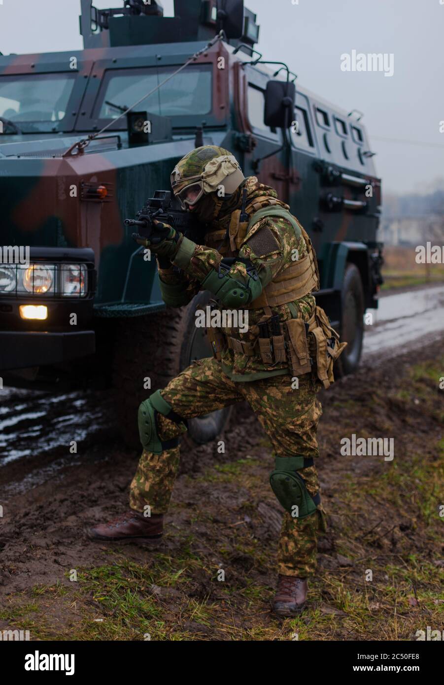 a soldier moves undercover with an armored car on the side of a road in the rain Stock Photo