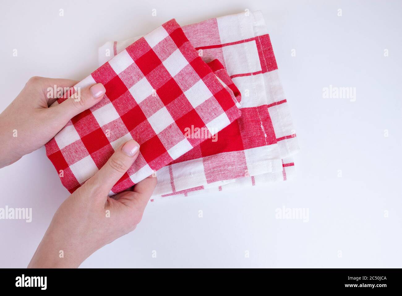 Woman hands holding red checkered kitchen towels. Two folded red and white tablecloth in female hands. Stock Photo
