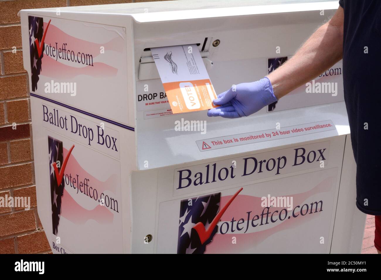 Gloved hand inserting ballot into ballot box in Jefferson County Colorado primary election in early voting in June 2020 Stock Photo