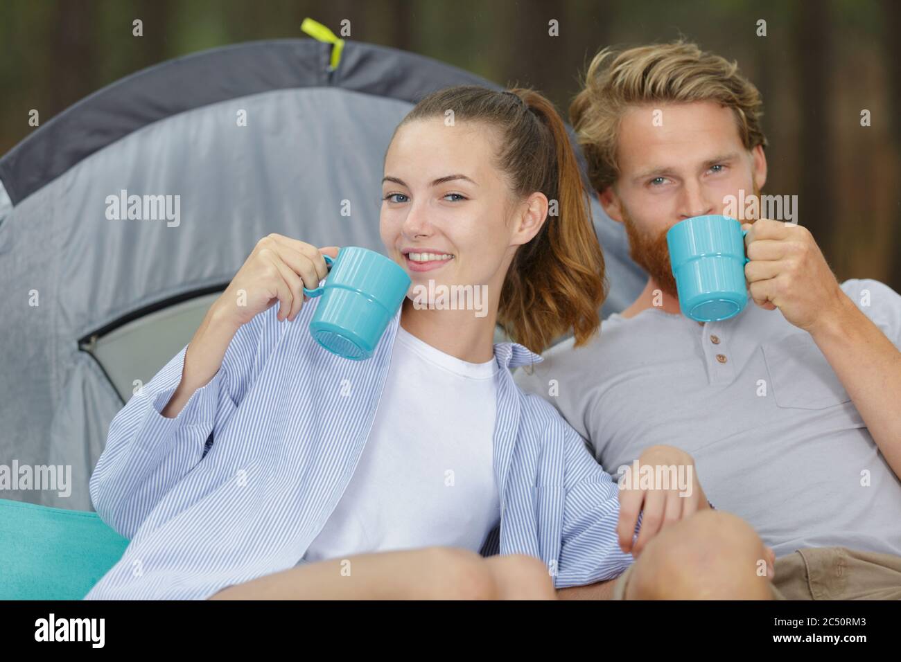 couple sitting in tent drinking hot drinks looking at view Stock Photo