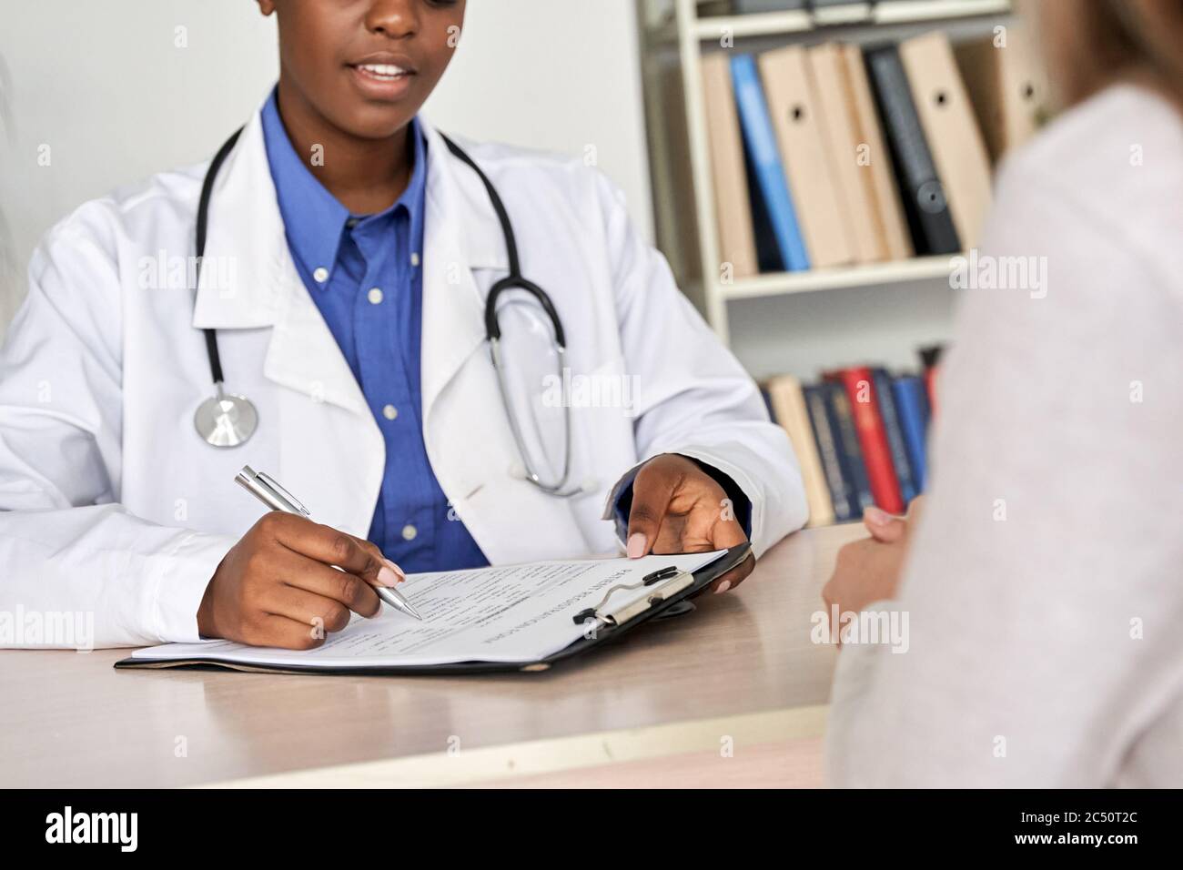 Female african doctor consult woman patient filling medical form at appointment. Stock Photo